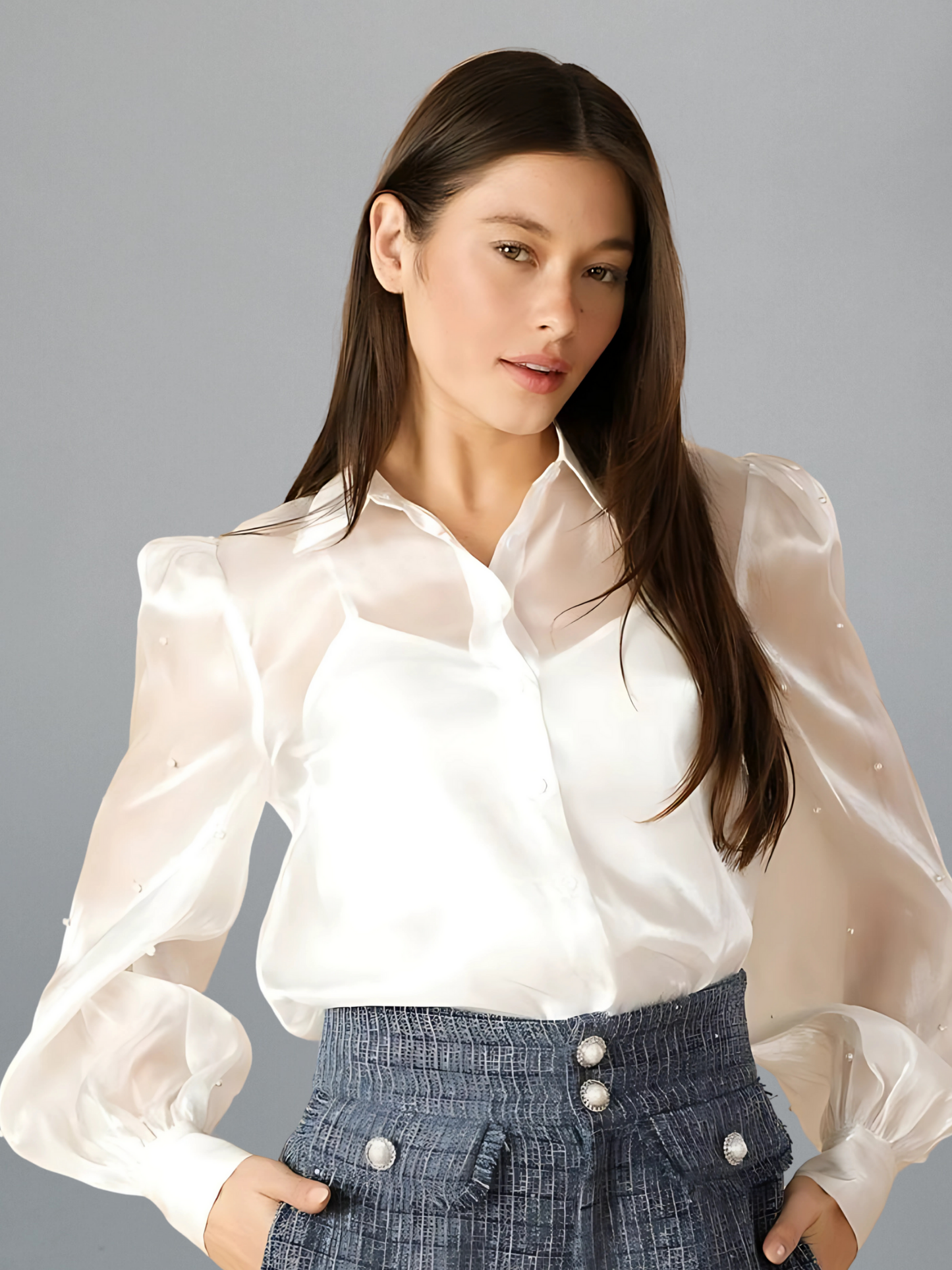Woman wearing a white blouse with sheer sleeves against a gray background