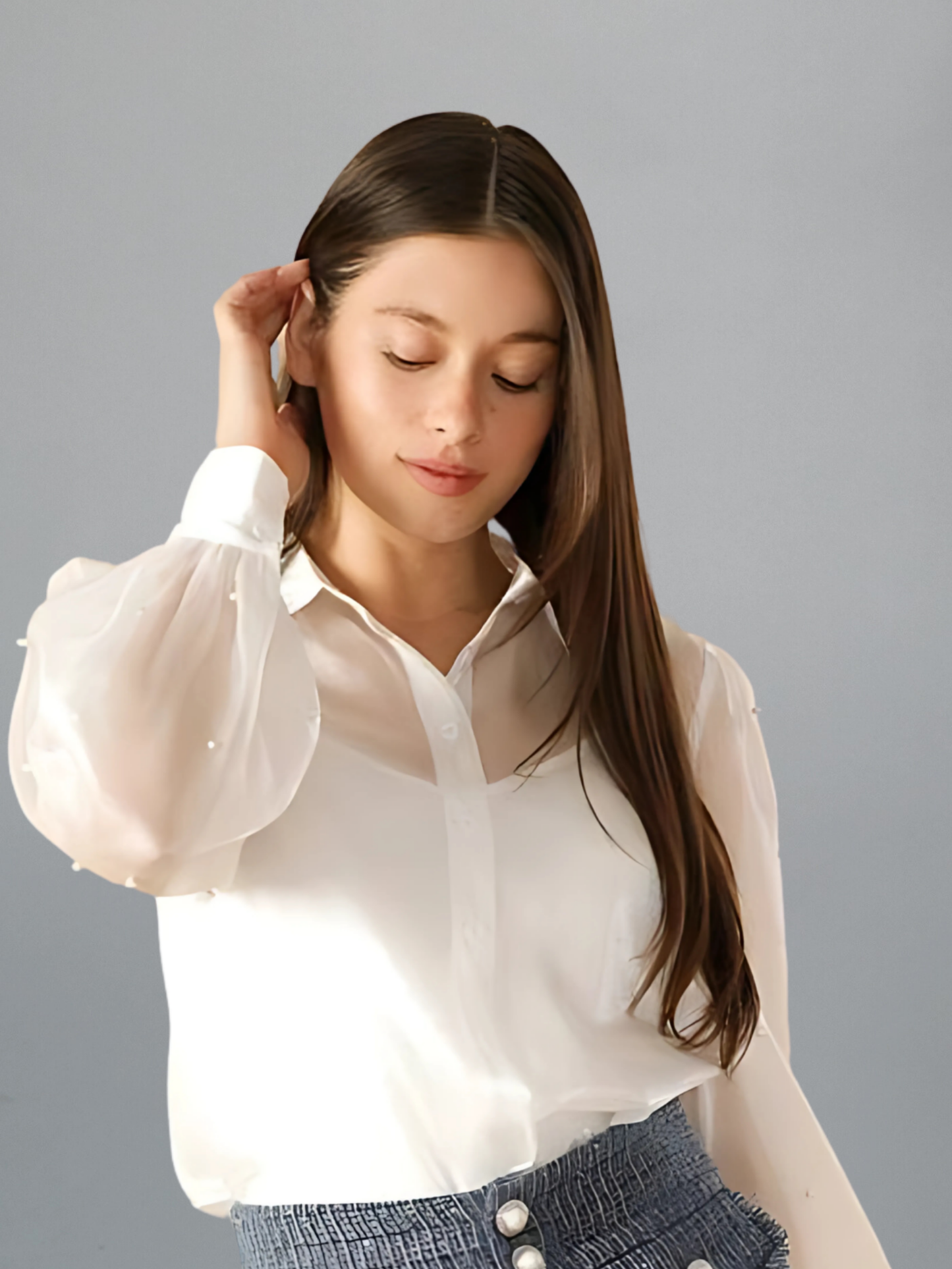 Woman wearing a white blouse with sheer sleeves against a gray background