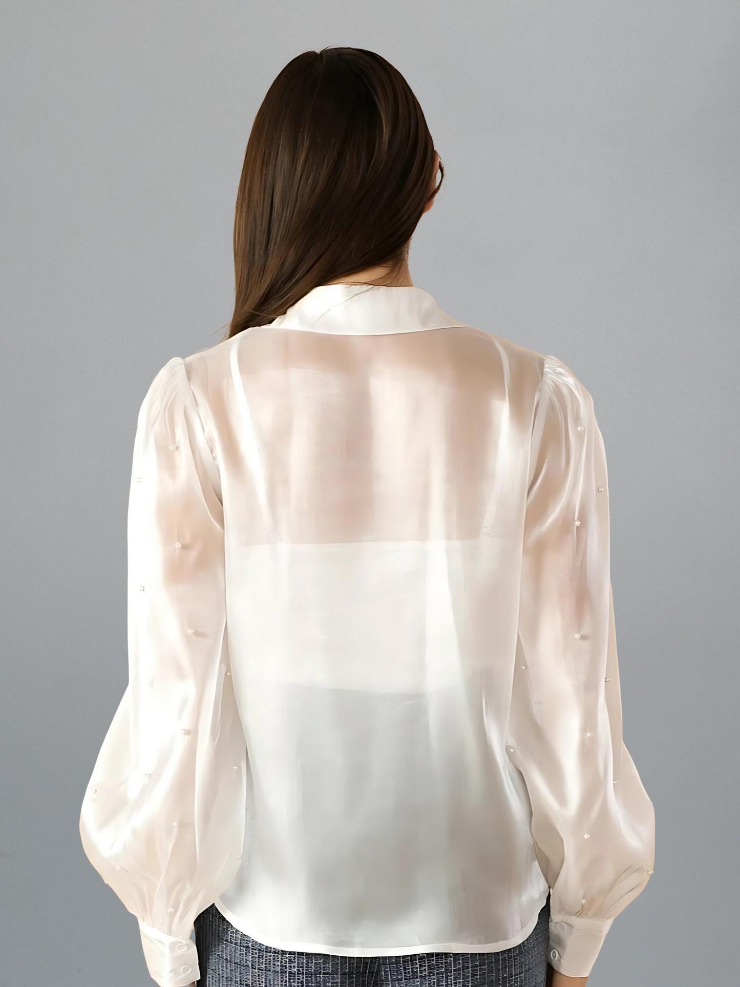Woman wearing a sheer white blouse against a gray background