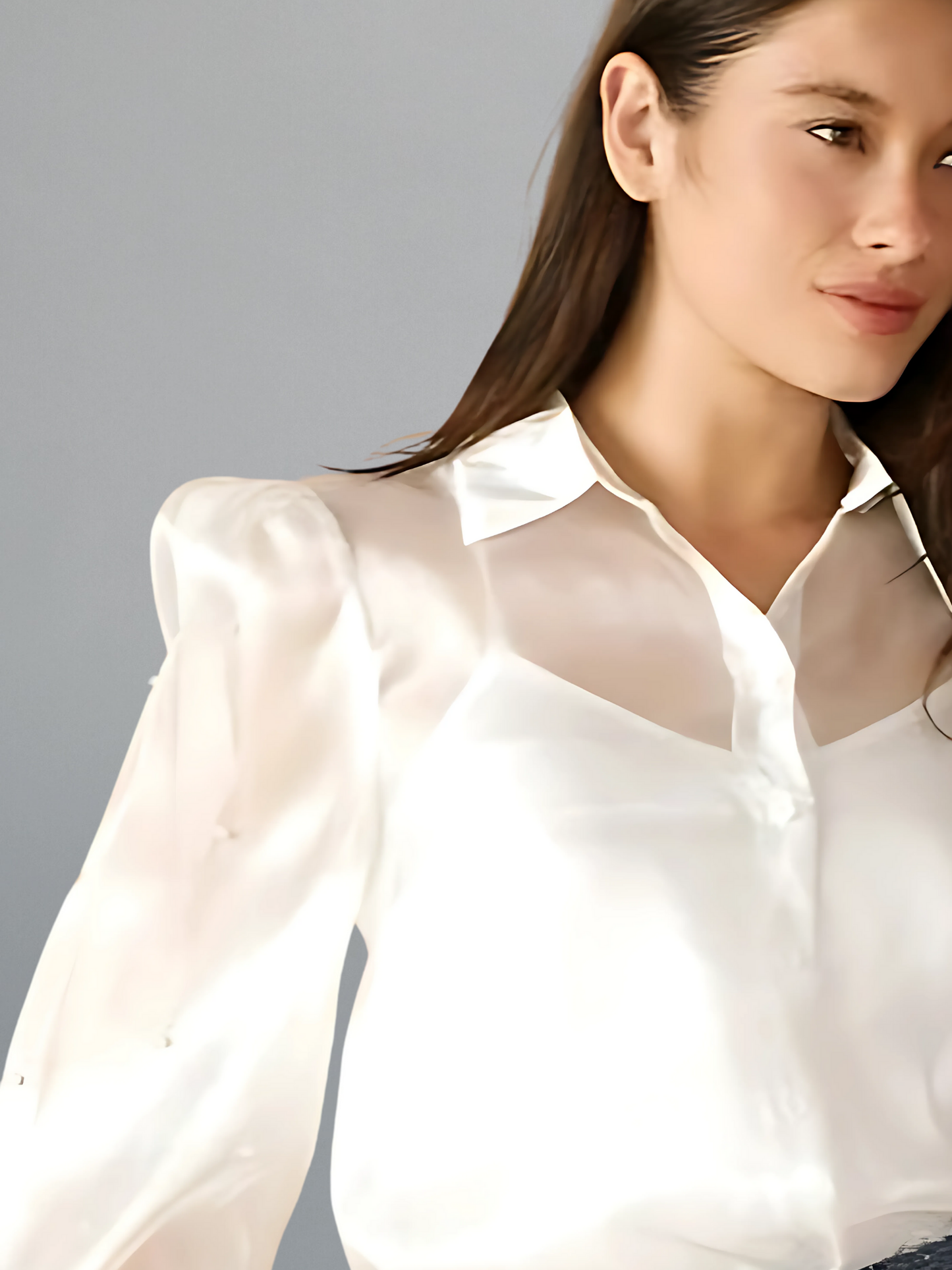Woman wearing a white blouse with sheer sleeves against a gray background