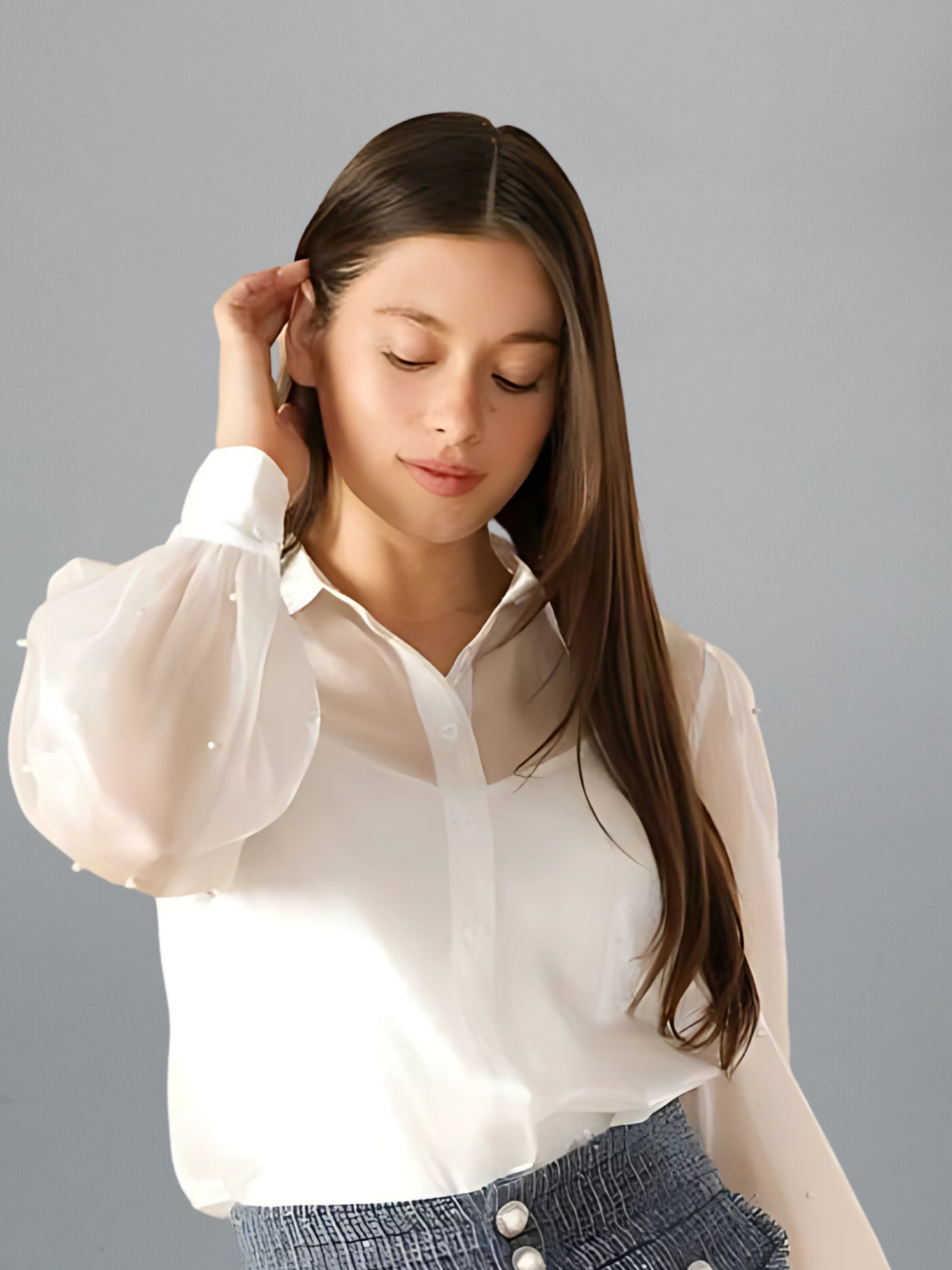 Woman wearing a white blouse with sheer sleeves against a gray background