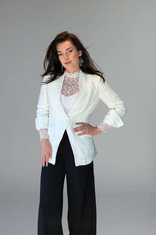 Woman wearing a white blazer over a lace top with black pants on a gray background